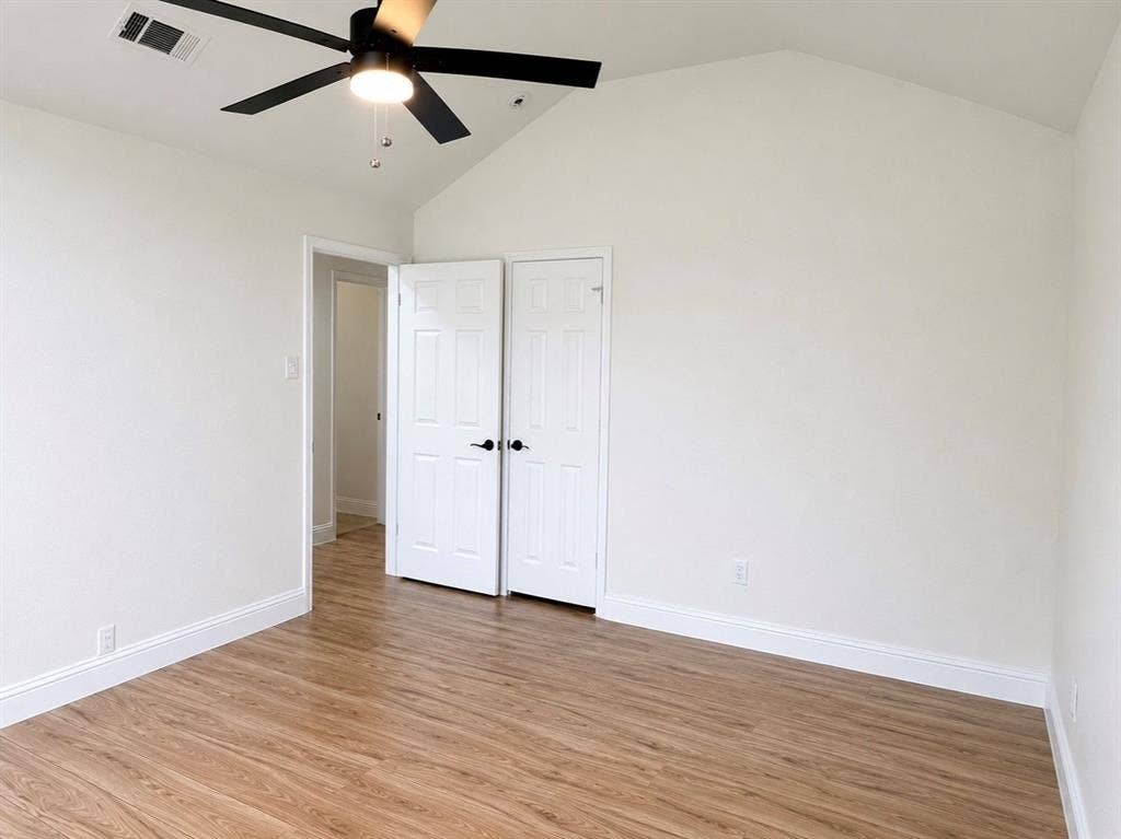2400 Waterloo Lane, Mesquite, TX 75181 Vaulted ceiling with a matte black four-blade ceiling fan, wood-finish flooring, and white paneled closet doors with matte black hardware