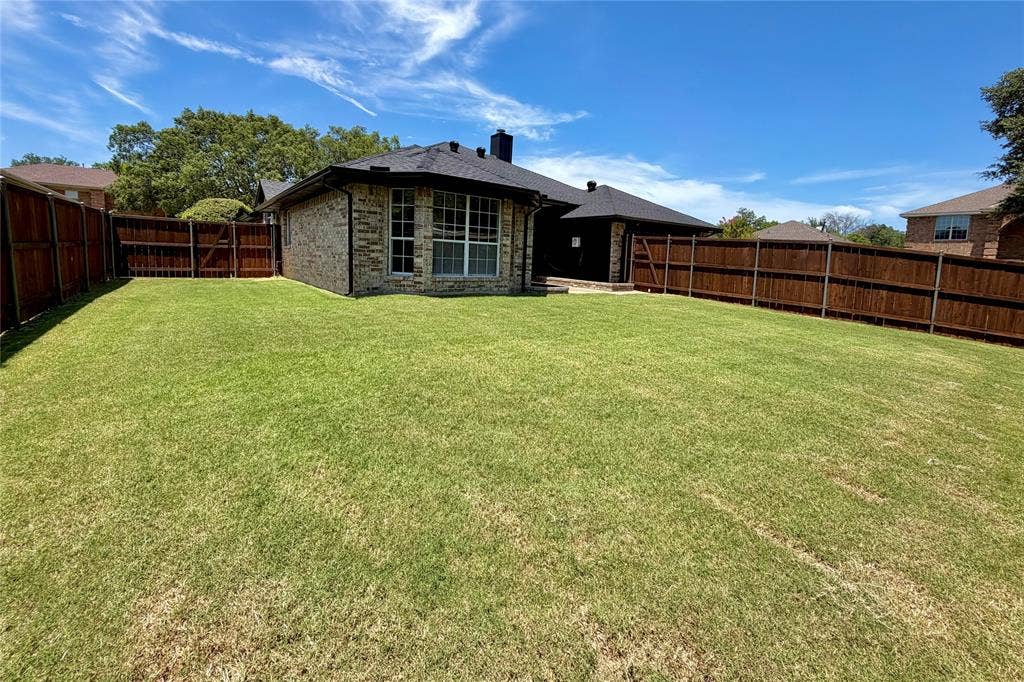 2400 Waterloo Lane, Mesquite, TX 75181 Expansive backyard featuring a manicured lawn, full-perimeter wood fencing, and brick exterior construction