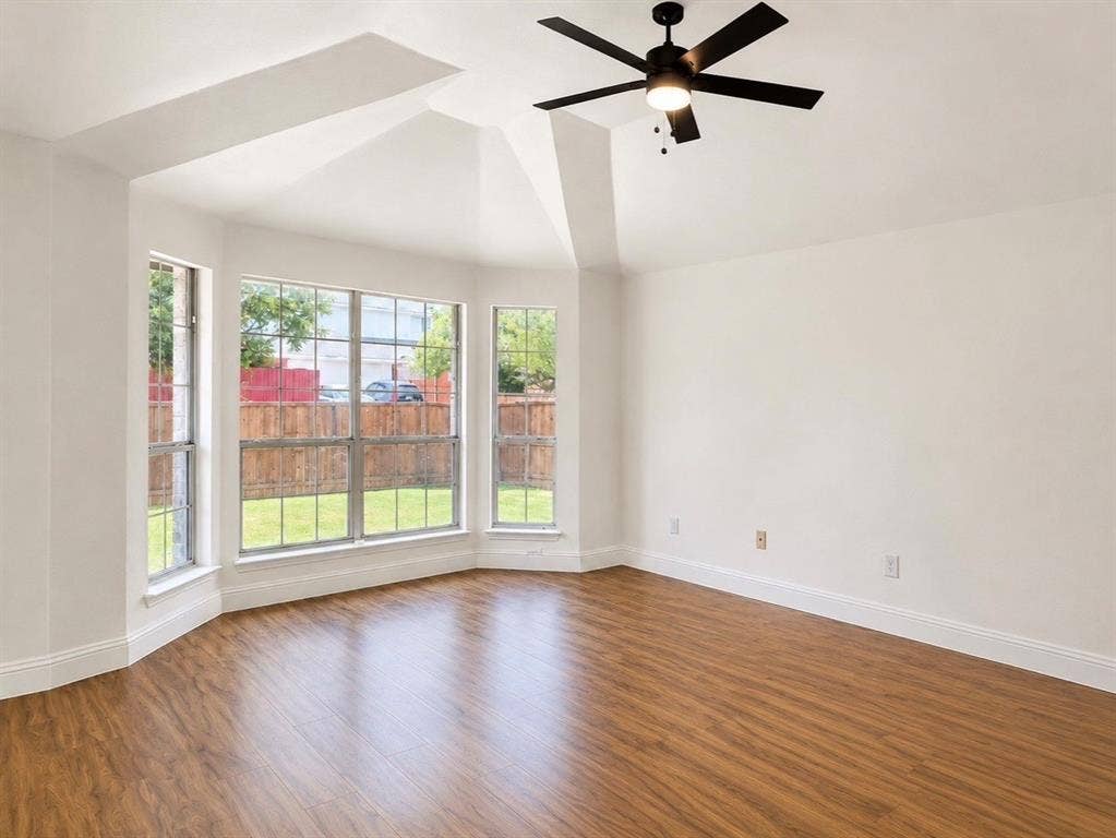 2400 Waterloo Lane, Mesquite, TX 75181 Vaulted ceiling featuring a central matte black ceiling fan with integrated lighting, wood-finish flooring, and a triple-pane bay window assembly