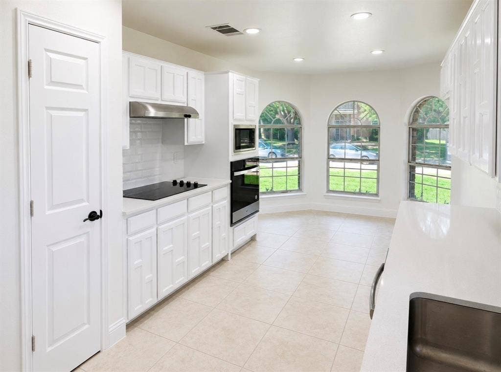 2400 Waterloo Lane, Mesquite, TX 75181 Kitchen featuring crisp white shaker-style cabinetry, quartz countertops, subway tile backsplash, stainless steel built-in appliances, and arched windows