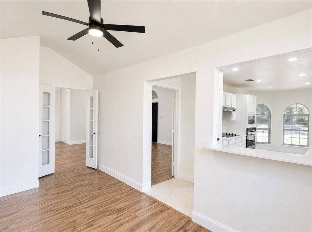 2400 Waterloo Lane, Mesquite, TX 75181 Vaulted ceilings featuring a matte black finish ceiling fan, white French doors, wood-finish flooring, and a kitchen pass-through window with a white countertop