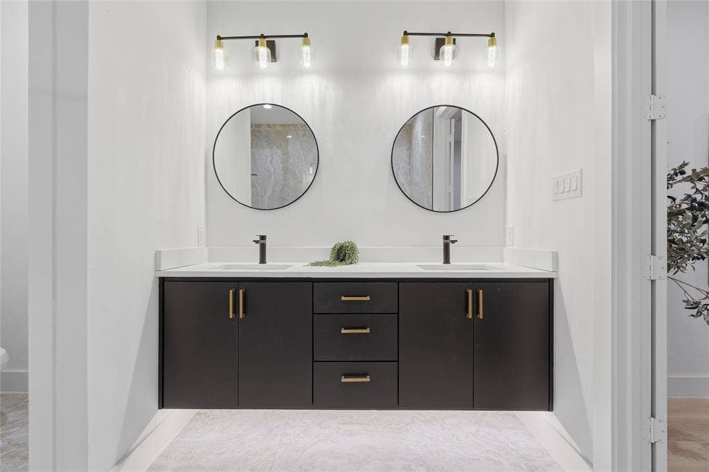 1834 Gallagher Street, Dallas, TX 75212 Floating dual-sink vanity with dark cabinetry, brass-tone hardware, white surface countertop, dual circular mirrors, and integrated wall-mounted light fixtures