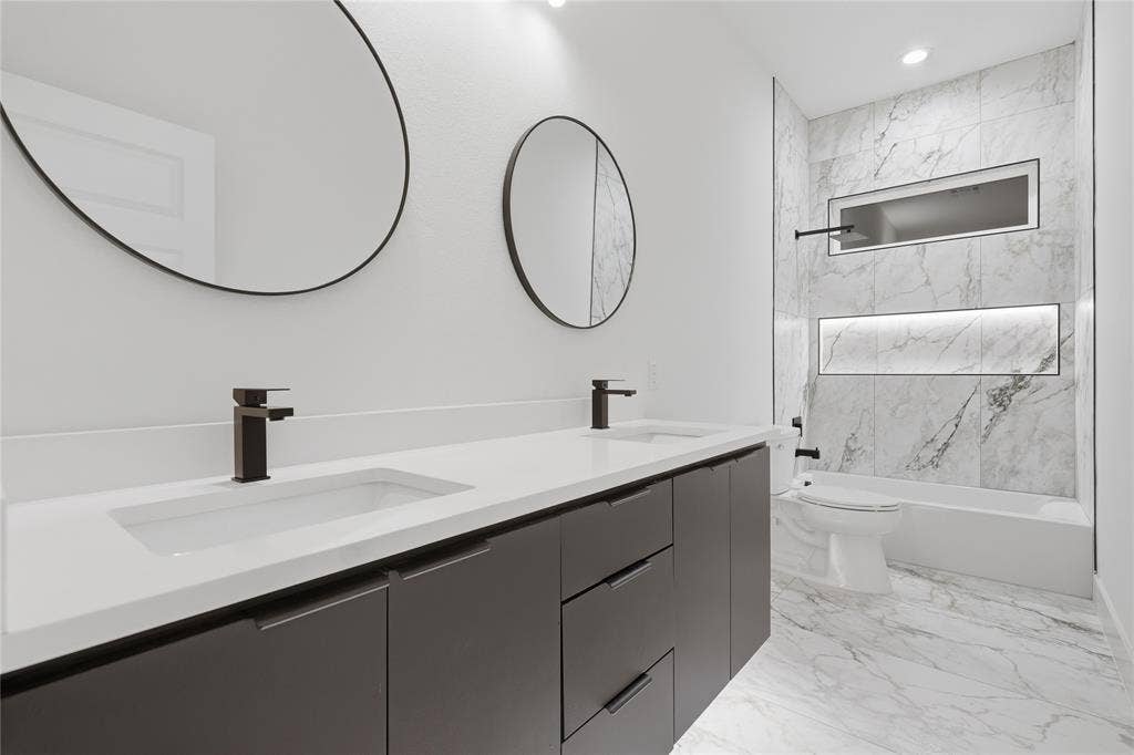 1834 Gallagher Street, Dallas, TX 75212 Double vanity featuring matte black faucets, circular mirrors, stone-finish tiling, and recessed wall shelving