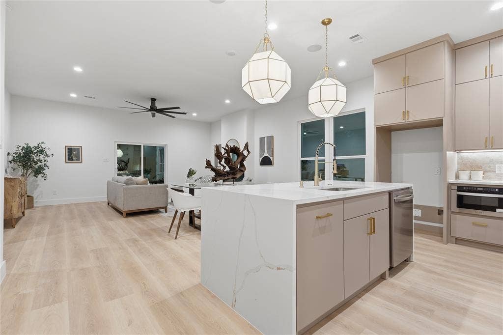 1834 Gallagher Street, Dallas, TX 75212 Kitchen featuring a waterfall-edge quartz island, neutral-toned cabinetry with brass hardware, stainless steel dishwasher, modern geometric pendant lighting, and wood-finish flooring