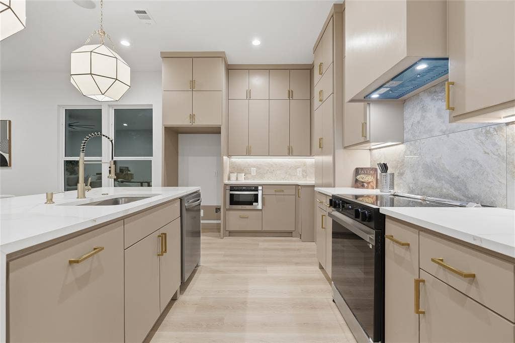 1834 Gallagher Street, Dallas, TX 75212 Kitchen featuring flat-panel cabinetry with gold-tone hardware, solid-surface countertops, stone-finish backsplash, built-in stainless steel appliances, and a geometric pendant light