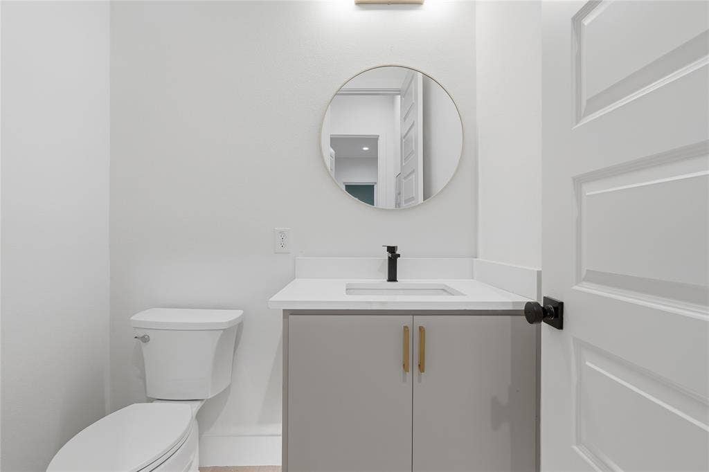 1834 Gallagher Street, Dallas, TX 75212 Vanity featuring a light gray cabinet with metal pulls, white countertop, integrated rectangular sink, matte black faucet, and circular wall-mounted mirror