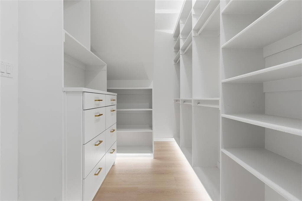 1834 Gallagher Street, Dallas, TX 75212 Custom storage organization featuring white built-in cabinetry, floor-to-ceiling shelving, integrated hanging rods, drawers with metallic pulls, and wood-finish flooring