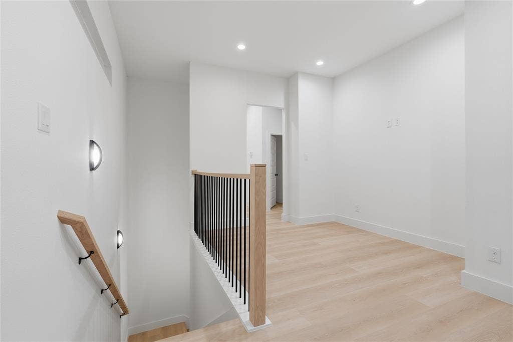 1834 Gallagher Street, Dallas, TX 75212 Interior hallway featuring wood-finish flooring, recessed lighting, matte black wall-mounted sconces, and a staircase railing with wood handrails and black vertical balusters