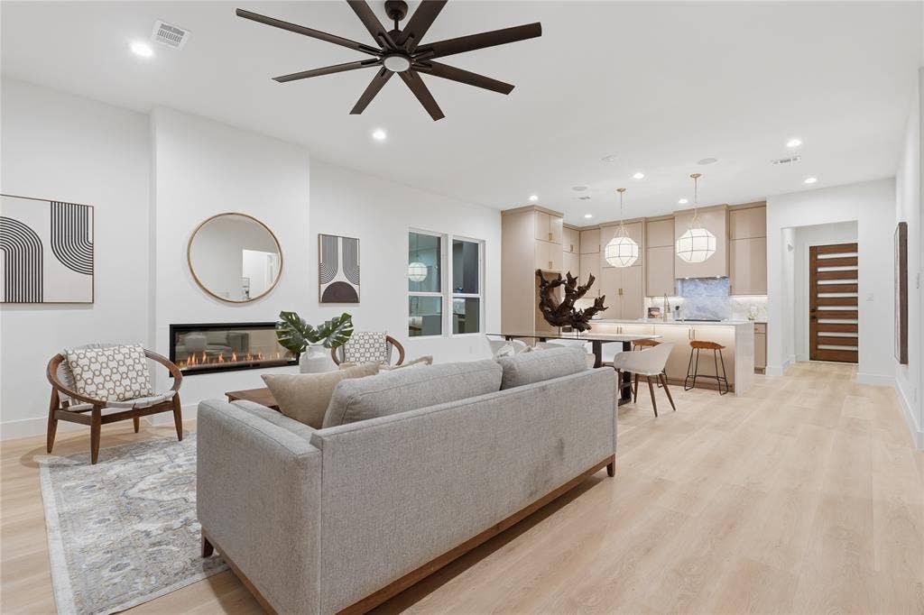 1834 Gallagher Street, Dallas, TX 75212 Open-concept living space featuring wood-finish flooring, a horizontal built-in fireplace, a ceiling fan with integrated lighting, recessed lighting, and kitchen cabinetry with a light stone-finish backsplash