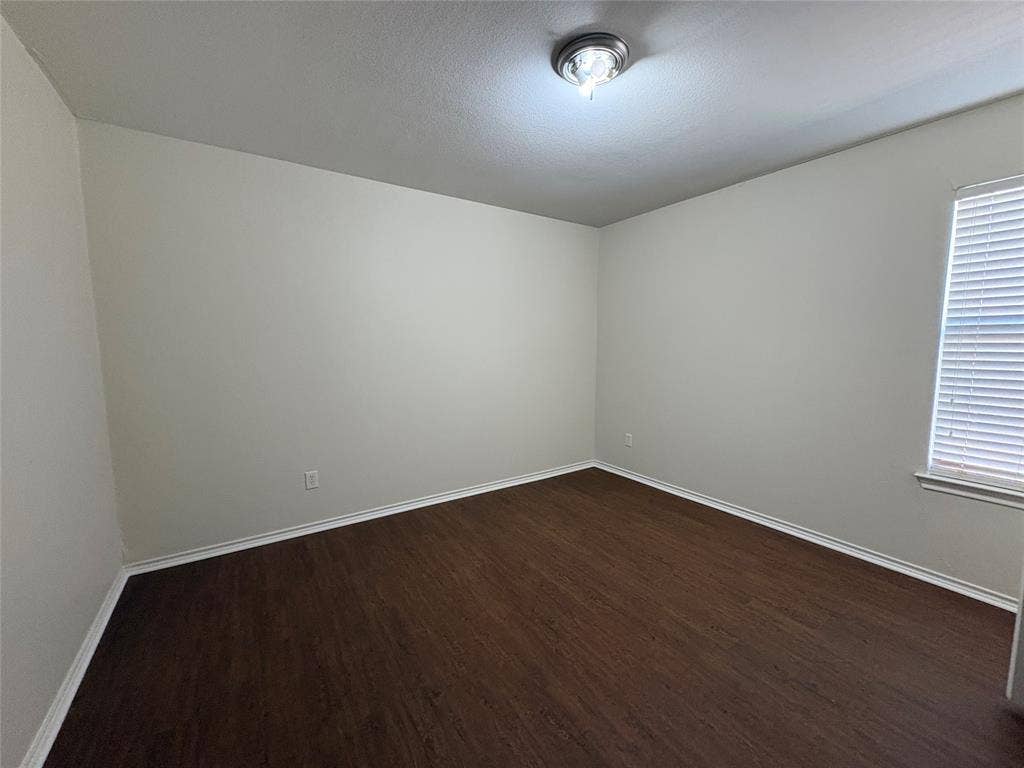 Room featuring neutral wall paint, wood-finish flooring, a flush-mount ceiling light fixture, and horizontal window blinds
