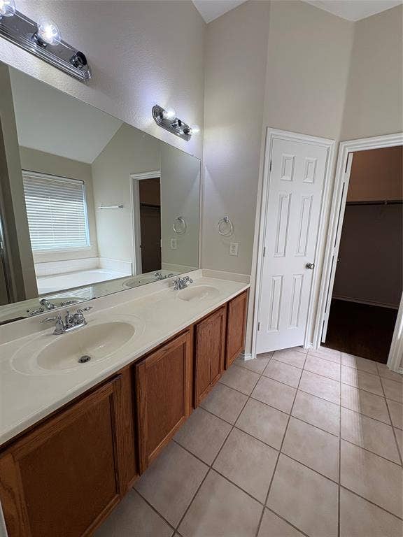 Dual-sink vanity with wood cabinetry and solid-surface countertop, full-width vanity mirror, two wall-mounted light fixtures, and tiled flooring