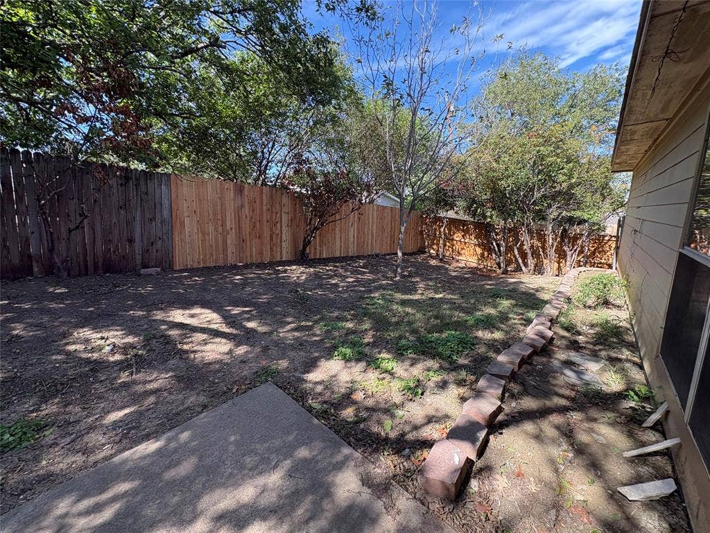 Rear yard featuring a concrete patio, wood privacy fencing, mature trees, and a stone-bordered garden bed
