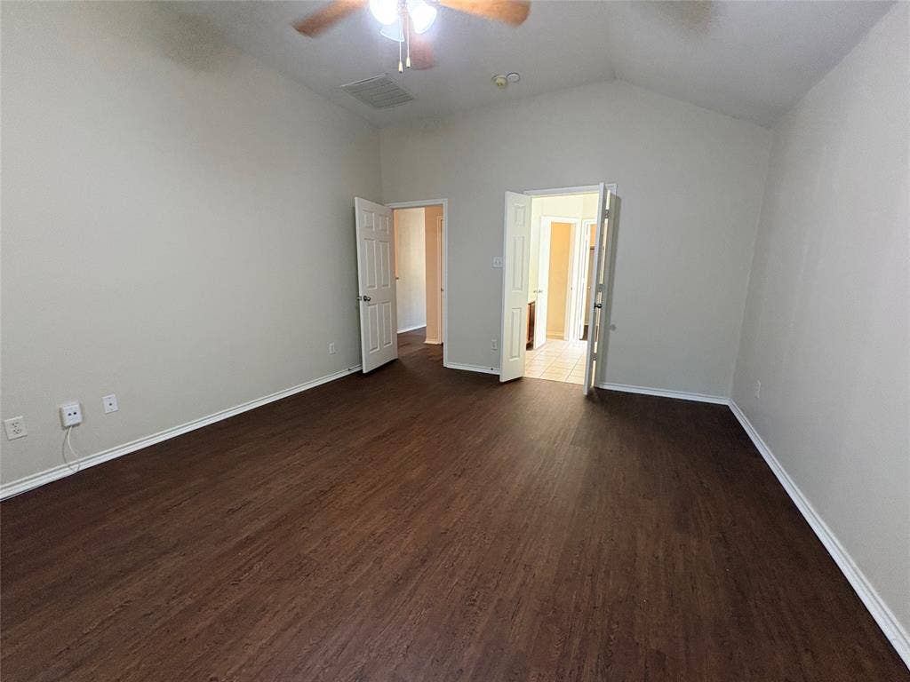 Vaulted ceiling room featuring dark wood-finish flooring, two sets of paneled interior doors, and a ceiling fan