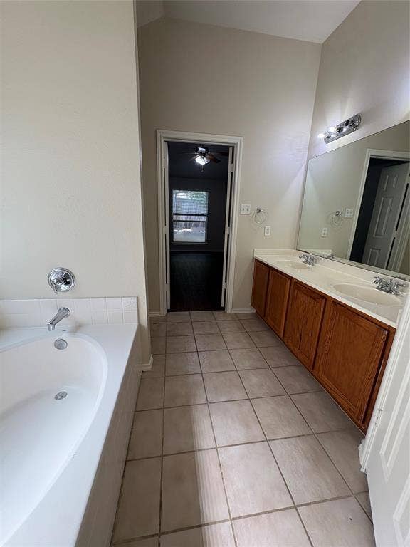 Dual-sink vanity with wood-finish cabinetry, tile flooring, large wall-mounted mirror, and a deep soaking tub