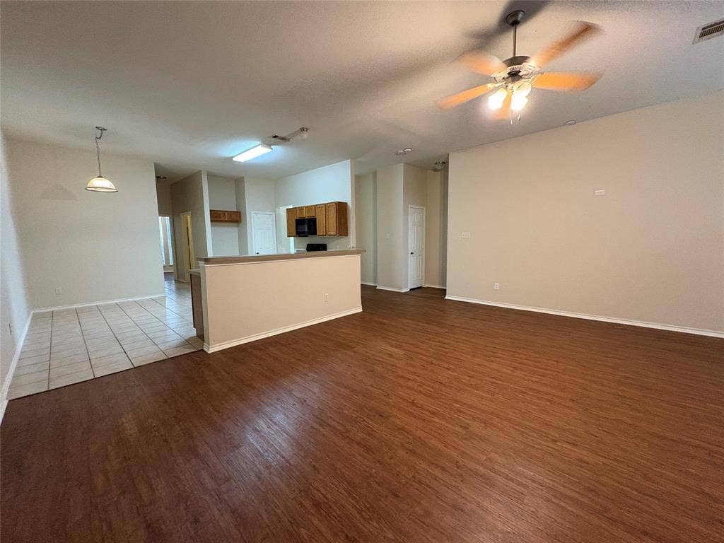 Open-concept interior featuring wood-finish flooring, ceramic tile flooring, kitchen cabinetry, a tiered breakfast bar, and an overhead ceiling fan with lighting