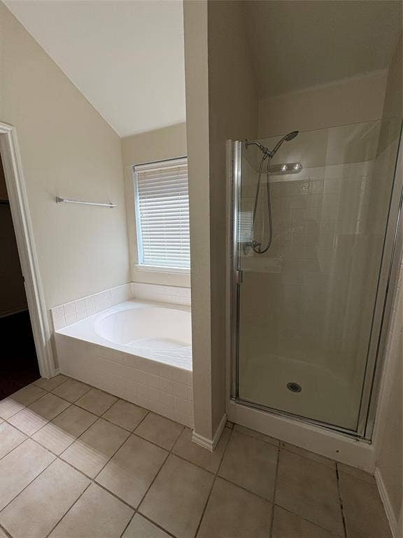 Bathroom featuring a tiled floor, soaking tub with white tile surround, and a glass-enclosed shower with a handheld showerhead
