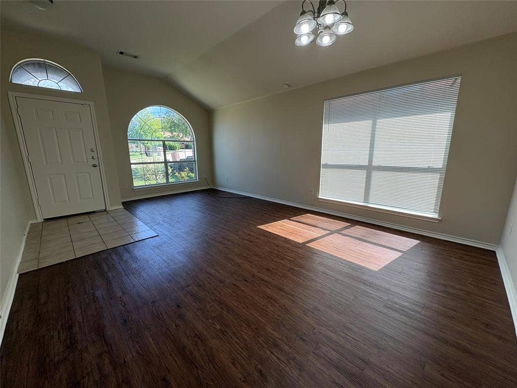 Open-concept space featuring vaulted ceilings, wood-finish flooring, a neutral color palette, arched window detailing, and an entry area with tile flooring