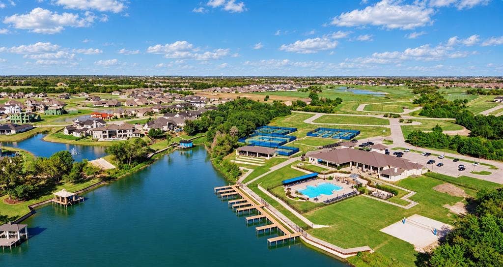 Aerial perspective of a community facility featuring a swimming pool, multiple tennis courts, a clubhouse, private docks, and a water feature