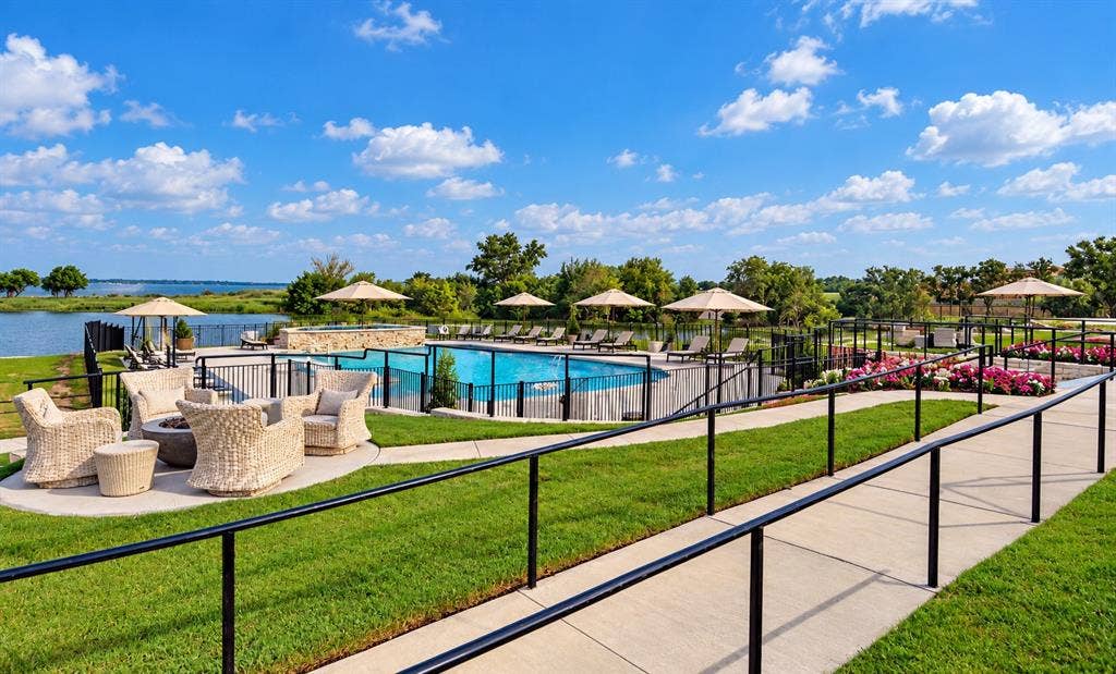 Outdoor pool area featuring a stone-accented hot tub, concrete patio, metal perimeter fencing, and landscaped garden beds