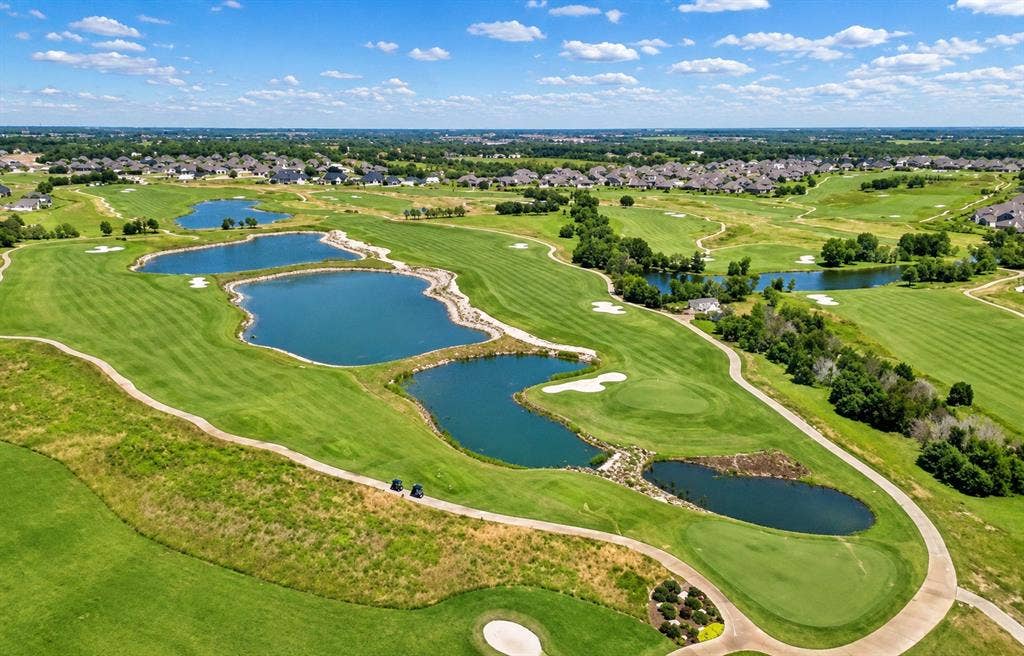 Aerial perspective of an expansive golf course featuring manicured fairways, integrated water hazards, sand bunkers, and paved cart paths