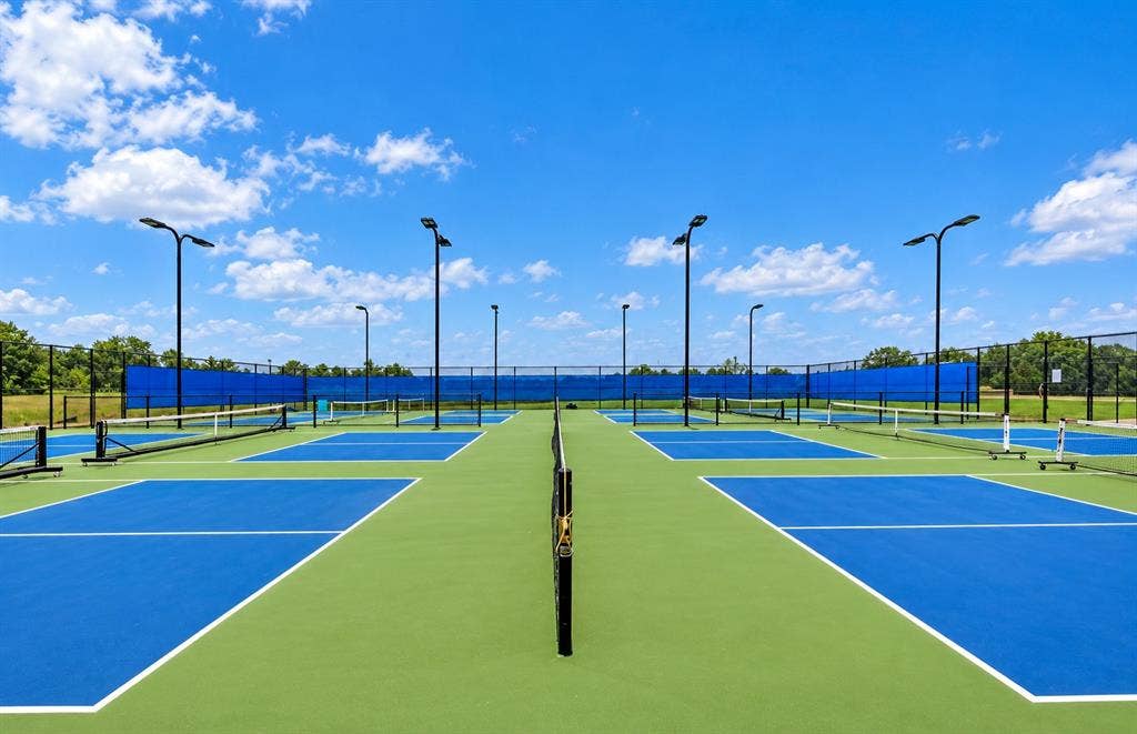 Multi-court athletic facility featuring hard surface playing areas, integrated net systems, perimeter fencing, and overhead court lighting