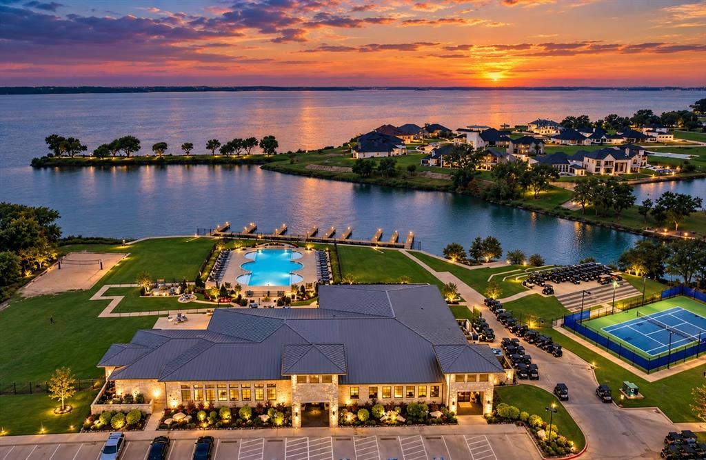Aerial perspective of property amenities featuring a multi-section swimming pool, hard-surfaced tennis court, private boat docks, and expansive waterfront lawn