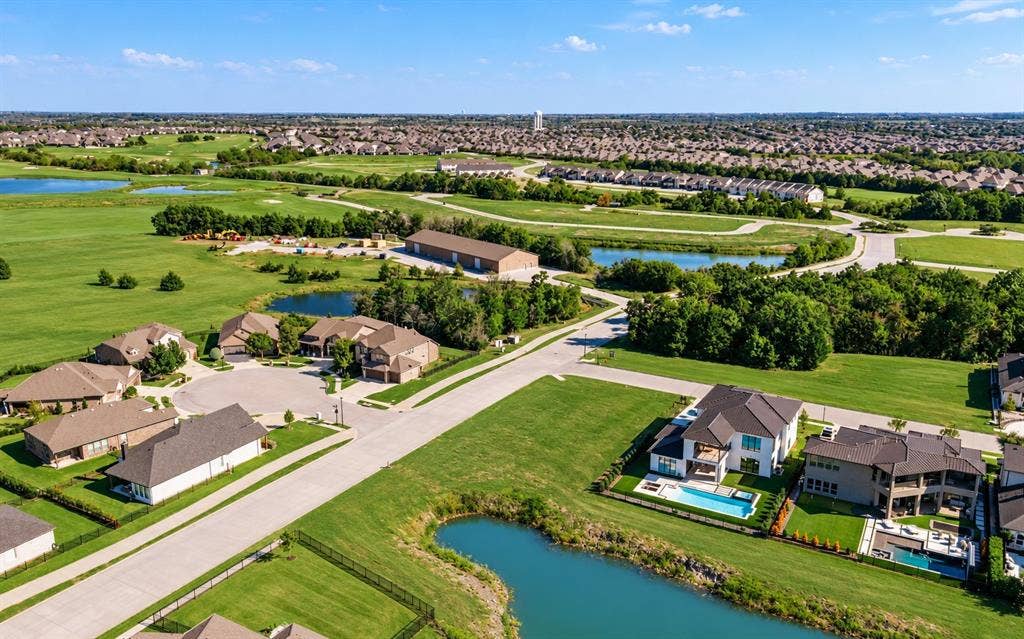 Aerial perspective of a residential neighborhood featuring expansive green space, manicured lawns, paved streets, and multiple water features