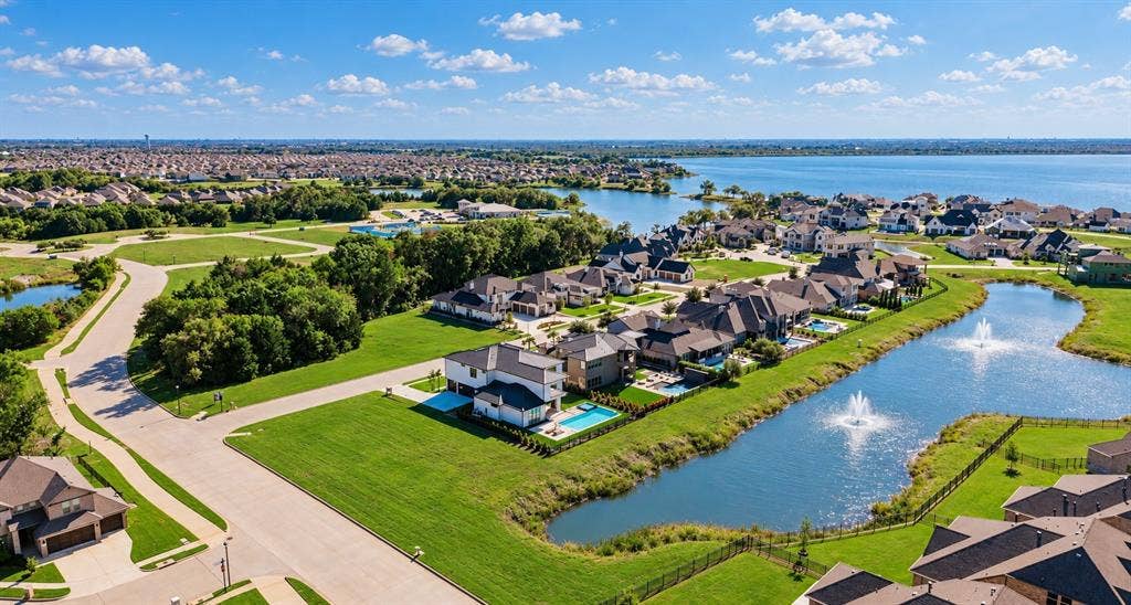 Aerial perspective featuring waterfront property with a private backyard swimming pool, landscaped lawn, and neighborhood pond with decorative fountains