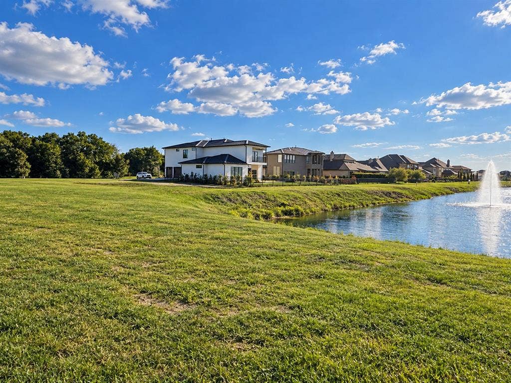 Expansive waterfront property featuring a manicured lawn, an active water fountain, and mature tree lines