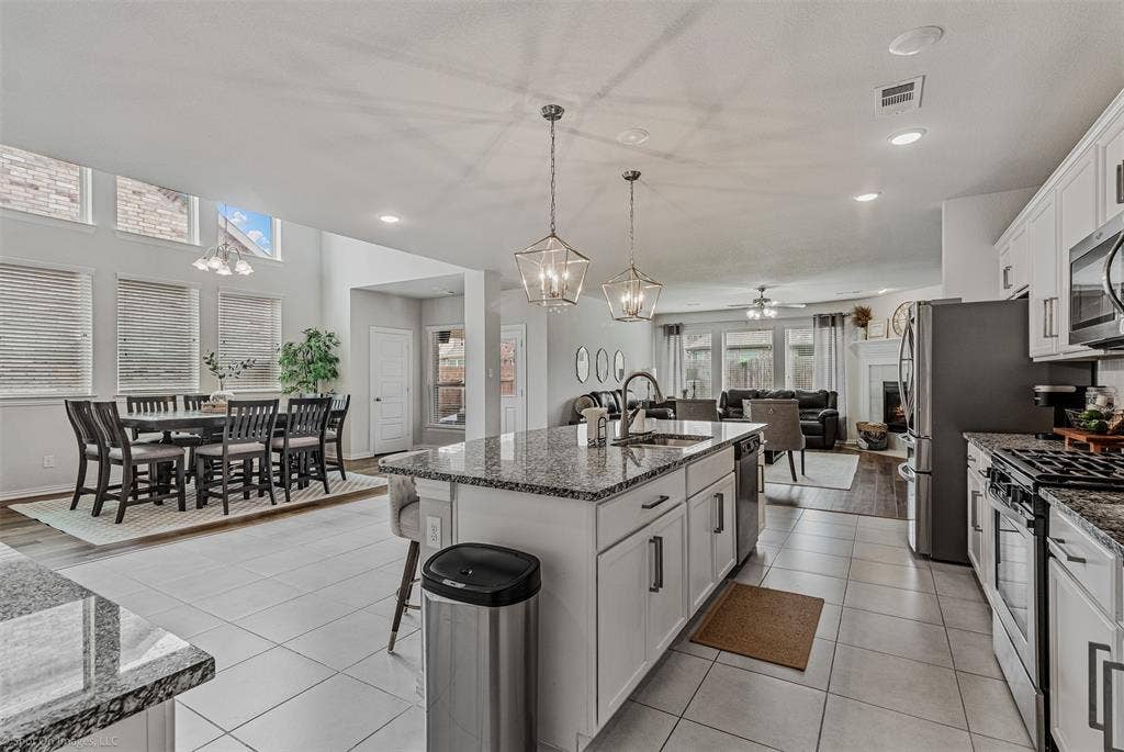 1612 Village Creek Drive, Forney, TX 75126 Kitchen with appliances with stainless steel finishes, a chandelier, open floor plan, dark stone counters, and a center island with sink