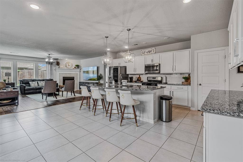 1612 Village Creek Drive, Forney, TX 75126 Kitchen with stainless steel appliances, a kitchen breakfast bar, a tiled fireplace, open floor plan, and white cabinets