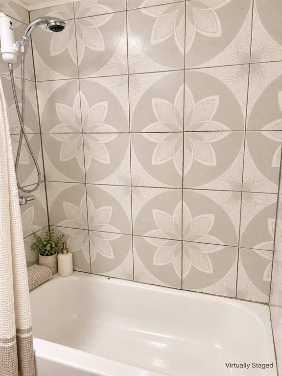 Bathtub surround featuring decorative, large-format floral patterned tile and a polished chrome handheld shower fixture