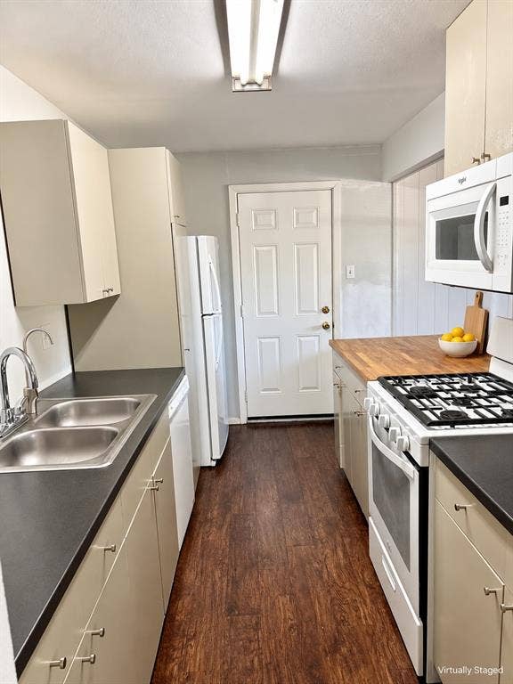 Galley kitchen featuring wood-finish flooring, dark solid-surface countertops, butcher-block prep area, white cabinetry, and built-in white appliances