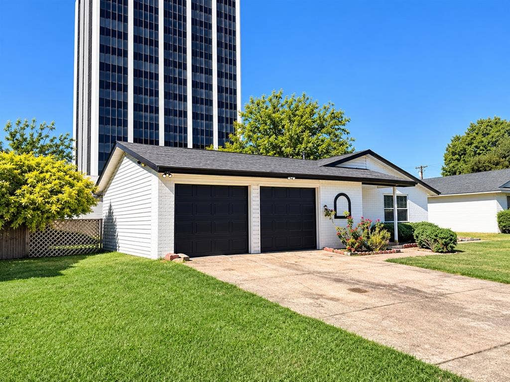 Exterior featuring white brick and siding, two-car garage with black paneled doors, and asphalt shingle roof