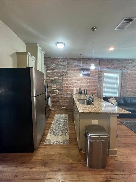 Kitchen featuring an exposed brick wall, stone-surface breakfast bar with an integrated stainless steel sink, wood-finish flooring, and pendant lighting
