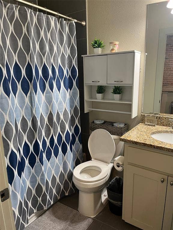 Bathroom featuring a vanity with a stone-surfaced countertop, built-in wall-mounted cabinetry, dark-toned wall tile, and a wall-mounted mirror