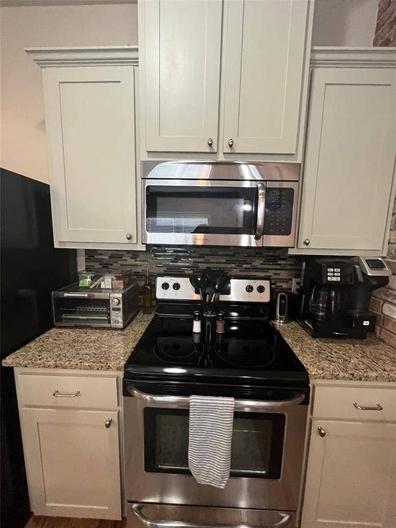 Off-white shaker-style cabinetry with stainless steel appliances, speckled stone countertop, and multi-tonal glass tile backsplash