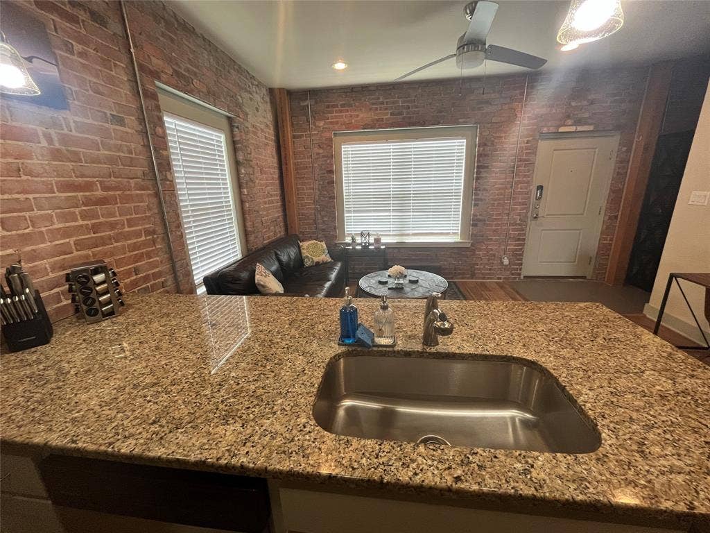 Exposed brick walls, kitchen island with natural stone countertop, stainless steel undermount sink, and recessed ceiling lighting