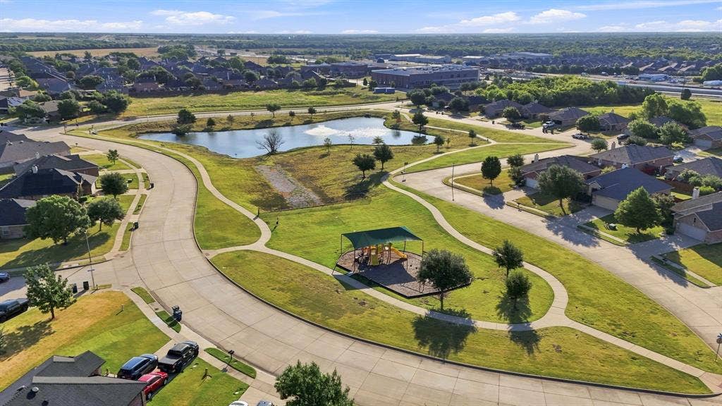 Aerial perspective of a community commons featuring a central pond, paved walking paths, landscaped green space, and a covered playground structure