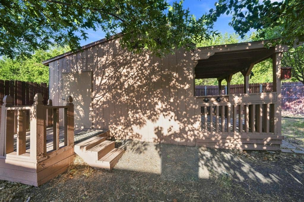 Outdoor structure featuring a covered porch, a side deck with stairs, vertical wood-finish siding, and a wood railing system