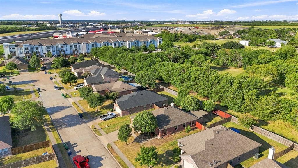 Aerial perspective of a residential neighborhood featuring asphalt paved streets, concrete sidewalks, single-story homes with shingle roofing, and mature perimeter trees