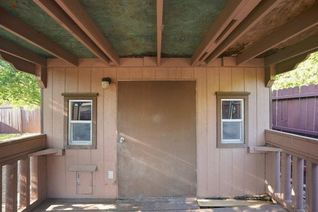 Covered outdoor structure featuring vertical wood siding, two windows, a central door, and protective wood railing