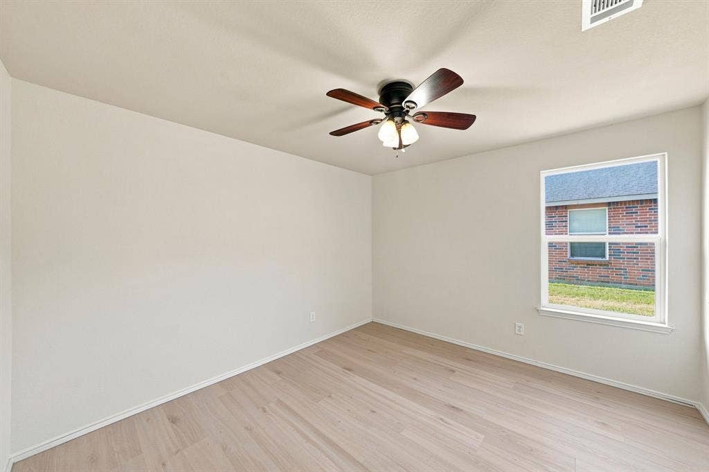 Neutral-toned interior space featuring wood-finish flooring, a ceiling fan with integrated lighting, and a single window