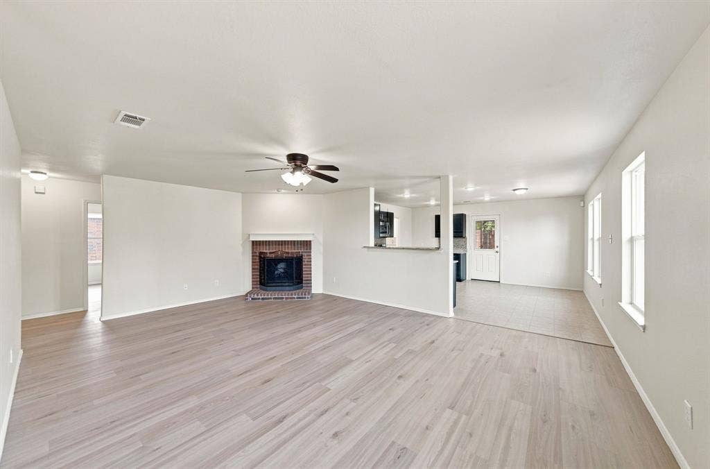 Open-concept living space featuring wood-finish flooring, a brick fireplace with a mantel, a ceiling fan, and tile flooring in the kitchen area
