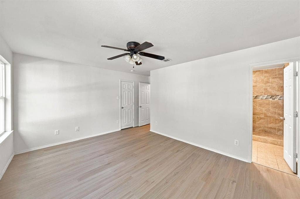 Wood-finish flooring, ceiling fan with integrated light fixture, two panel-style interior doors, and tiled shower enclosure