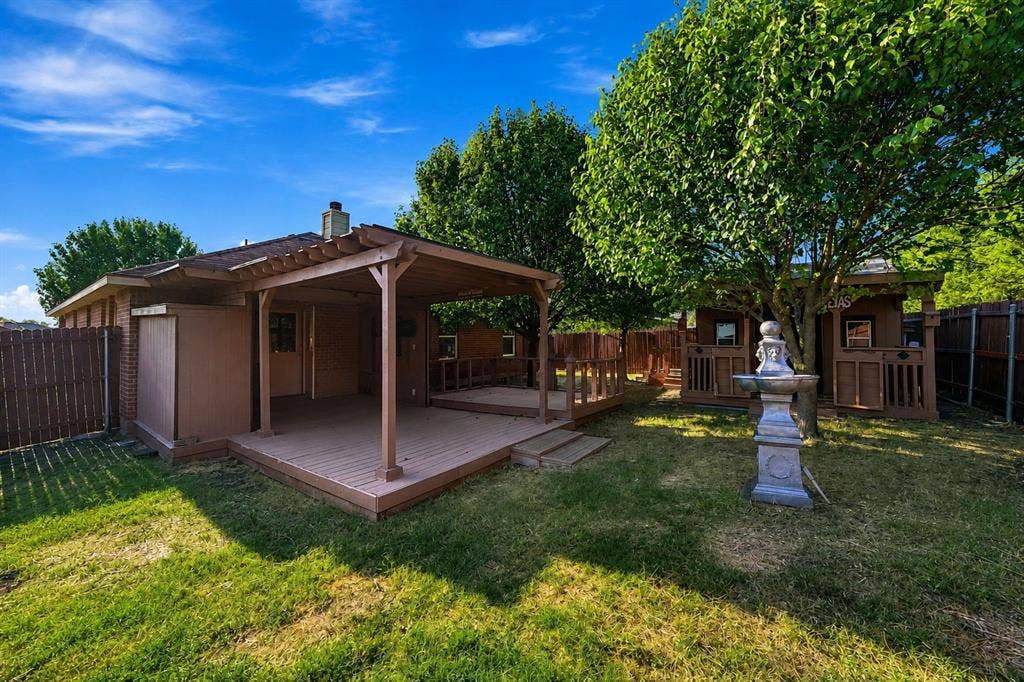 Backyard featuring a wood-frame pergola, elevated wood deck, lawn space, decorative fountain, and wood perimeter fencing