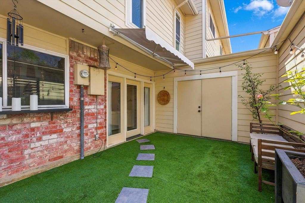 1955 Shorewood Drive, Grapevine, TX 76051 Private patio area featuring a brick facade, synthetic turf, stone paver path, retractable awning, and double-door storage