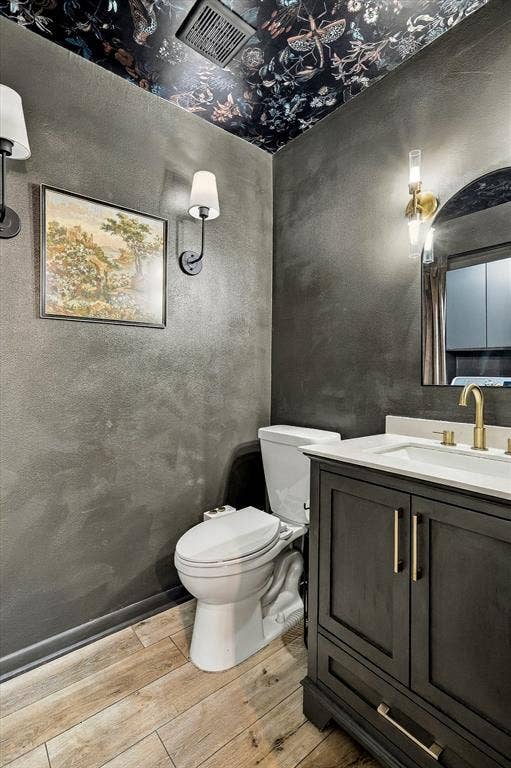 1955 Shorewood Drive, Grapevine, TX 76051 Bathroom featuring a dark vanity with a light-colored countertop, brass-finish faucet and hardware, wood-finish flooring, and a patterned ceiling treatment with dual wall-mounted light fixtures