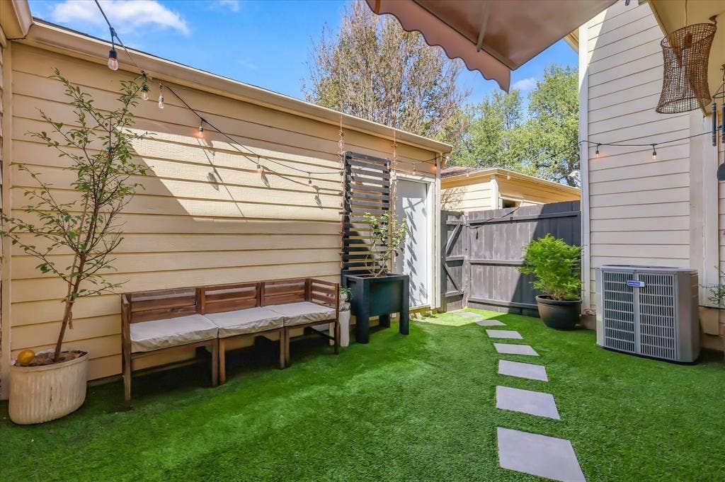 1955 Shorewood Drive, Grapevine, TX 76051 Outdoor courtyard featuring synthetic turf, square stone paver pathway, retractable wall-mounted awning, vertical wood privacy screening, and horizontal lap siding