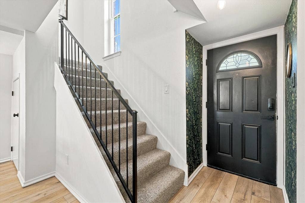 1955 Shorewood Drive, Grapevine, TX 76051 Entryway featuring a black four-panel door with arched transom window, metal handrail, staircase with carpeted treads, and wood-finish flooring